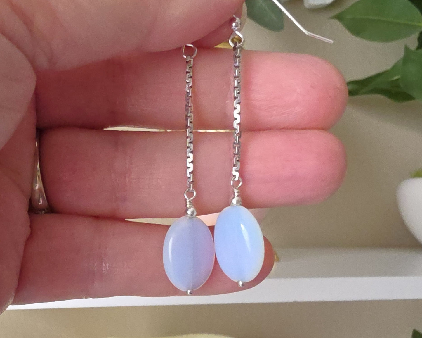 Long Sterling Silver Opaliate earrings with oval shaped stones dangling from long chains displayed in hand 