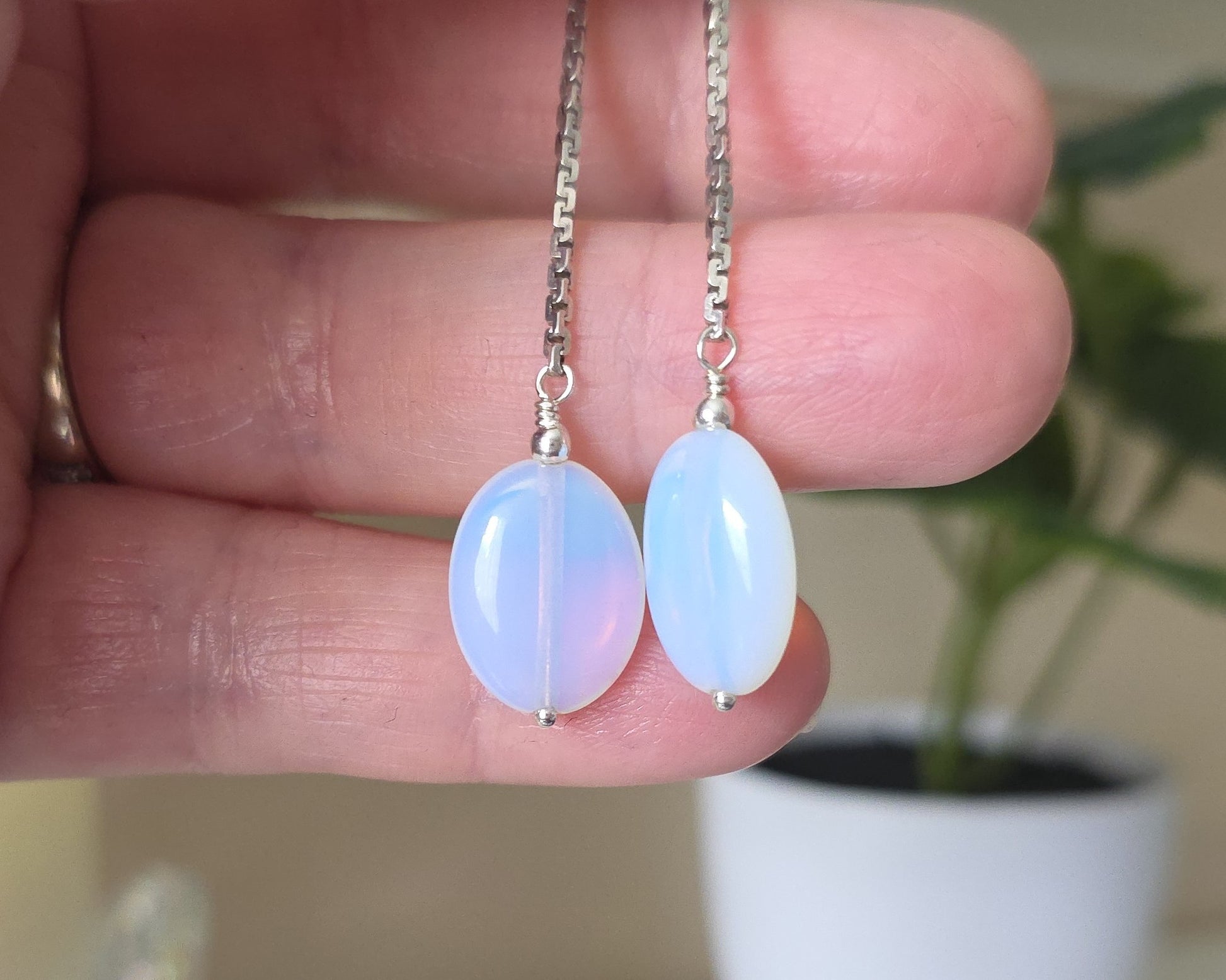 Long Sterling Silver Opaliate earrings with oval shaped stones dangling from long chains displayed in hand 