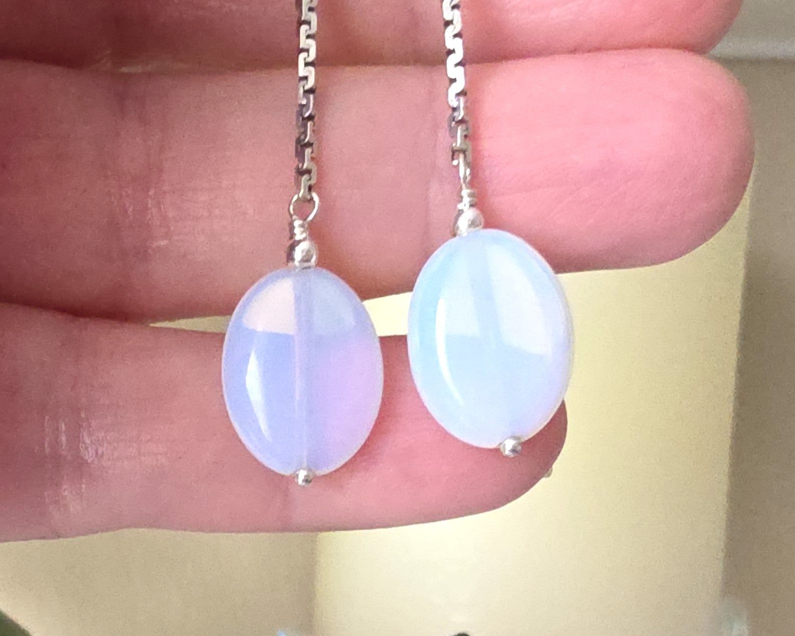 Long Sterling Silver Opaliate earrings with oval shaped stones dangling from long chains displayed in hand 