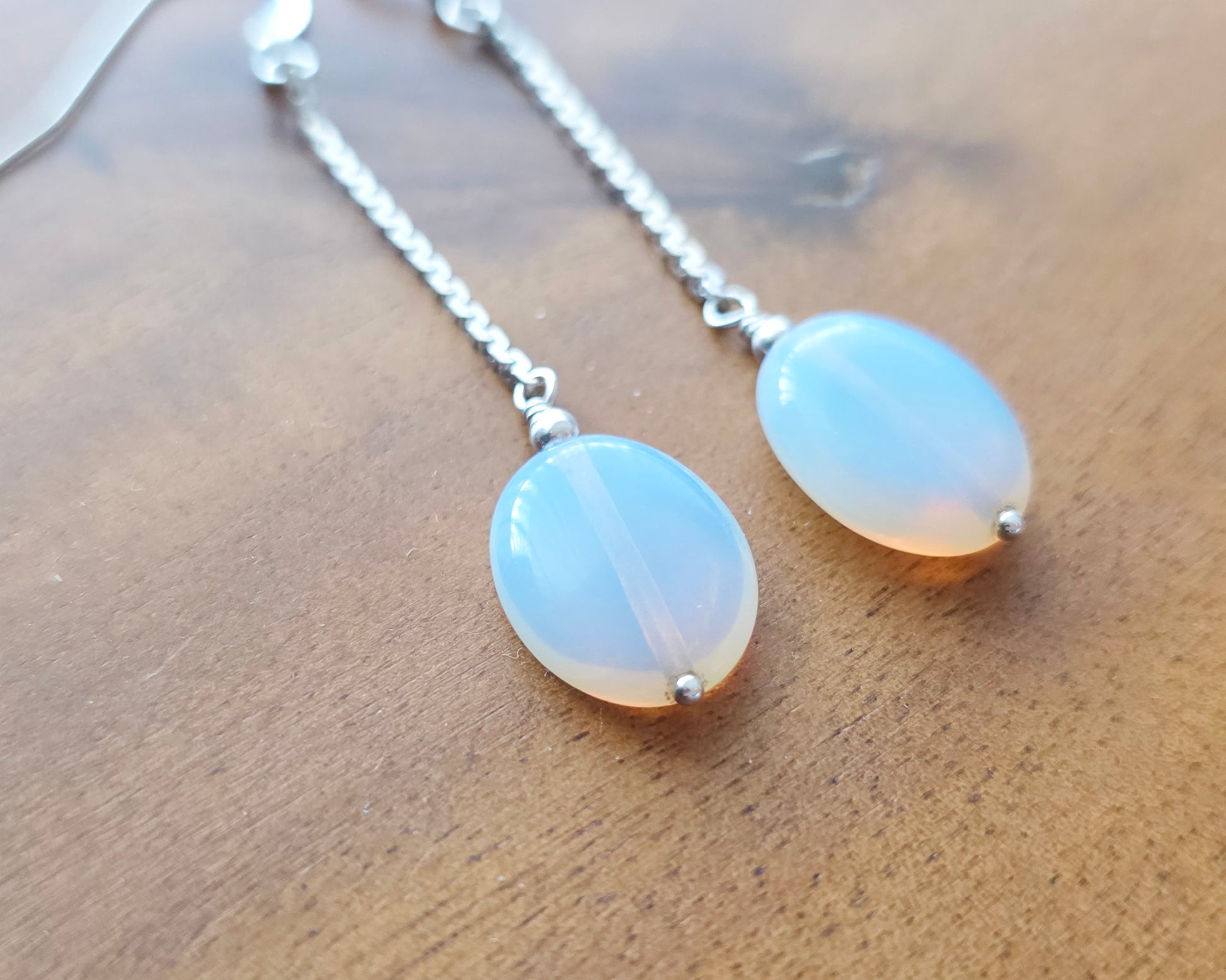 Long Sterling Silver Opaliate earrings with oval shaped stones dangling from long chains on wood background 