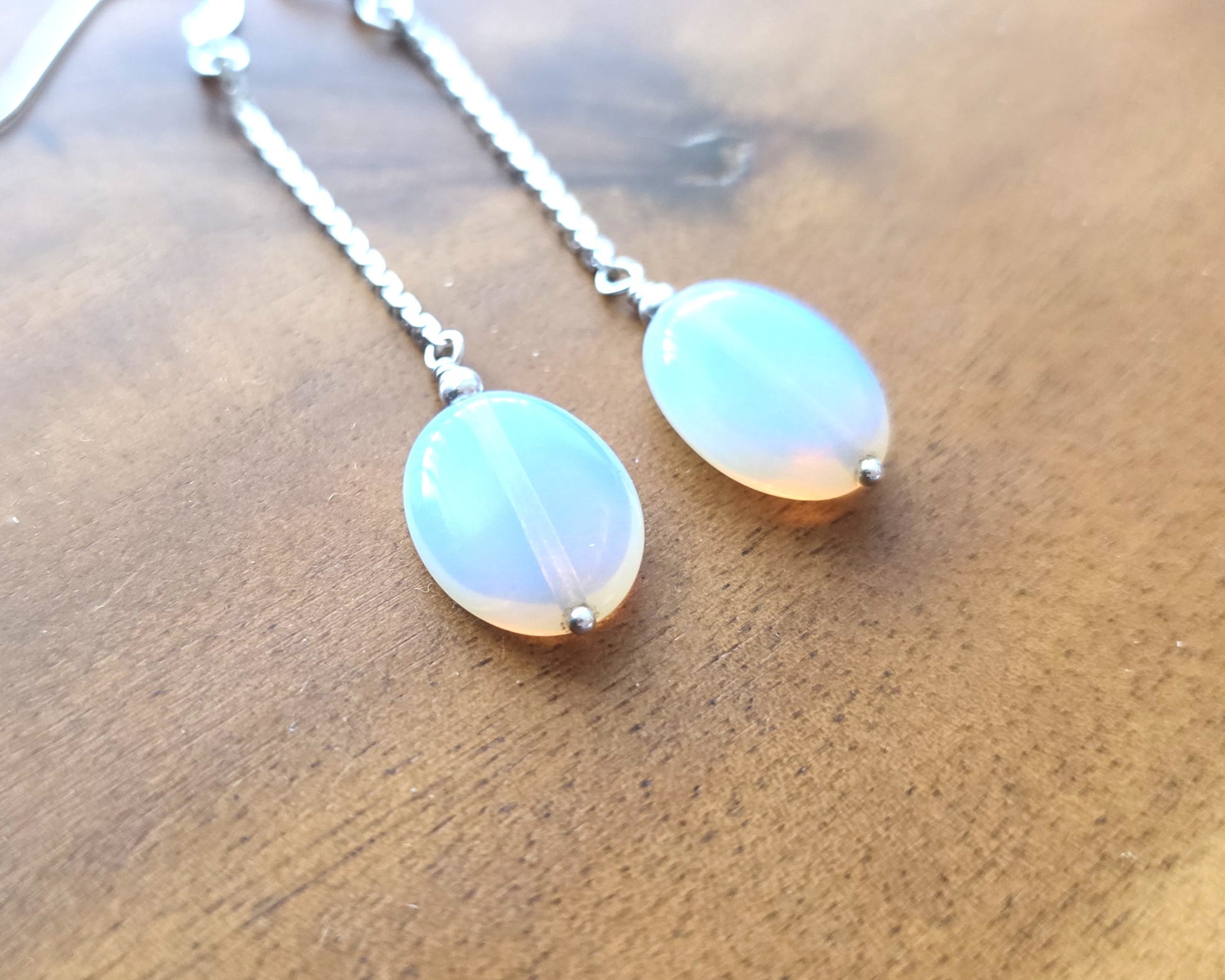Long Sterling Silver Opaliate earrings with oval shaped stones dangling from long chains on wood background 