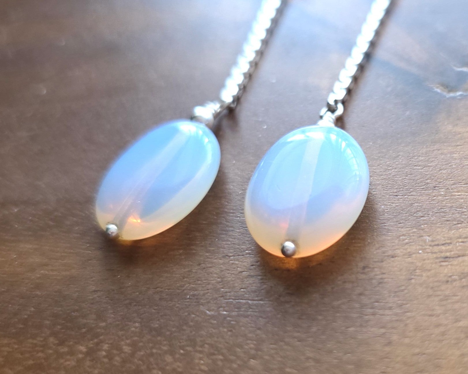 Long Sterling Silver Opaliate earrings with oval shaped stones dangling from long chains on wood background 