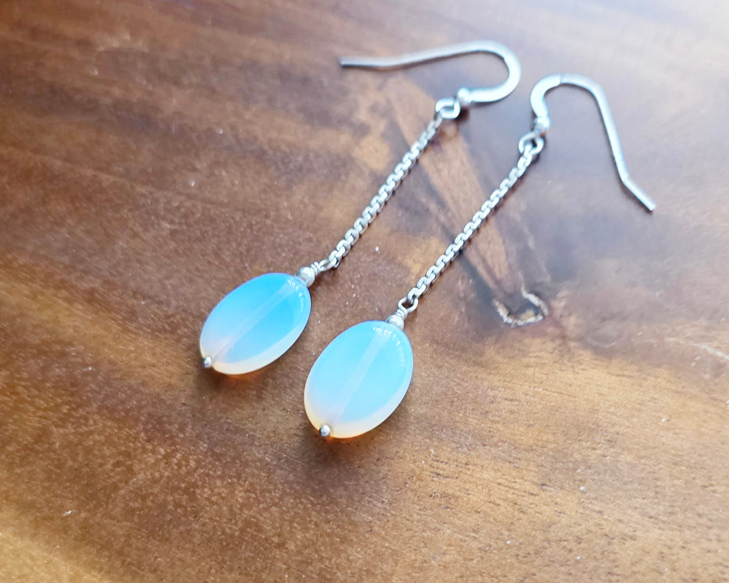 Long Sterling Silver Opaliate earrings with oval shaped stones dangling from long chains on wood background 