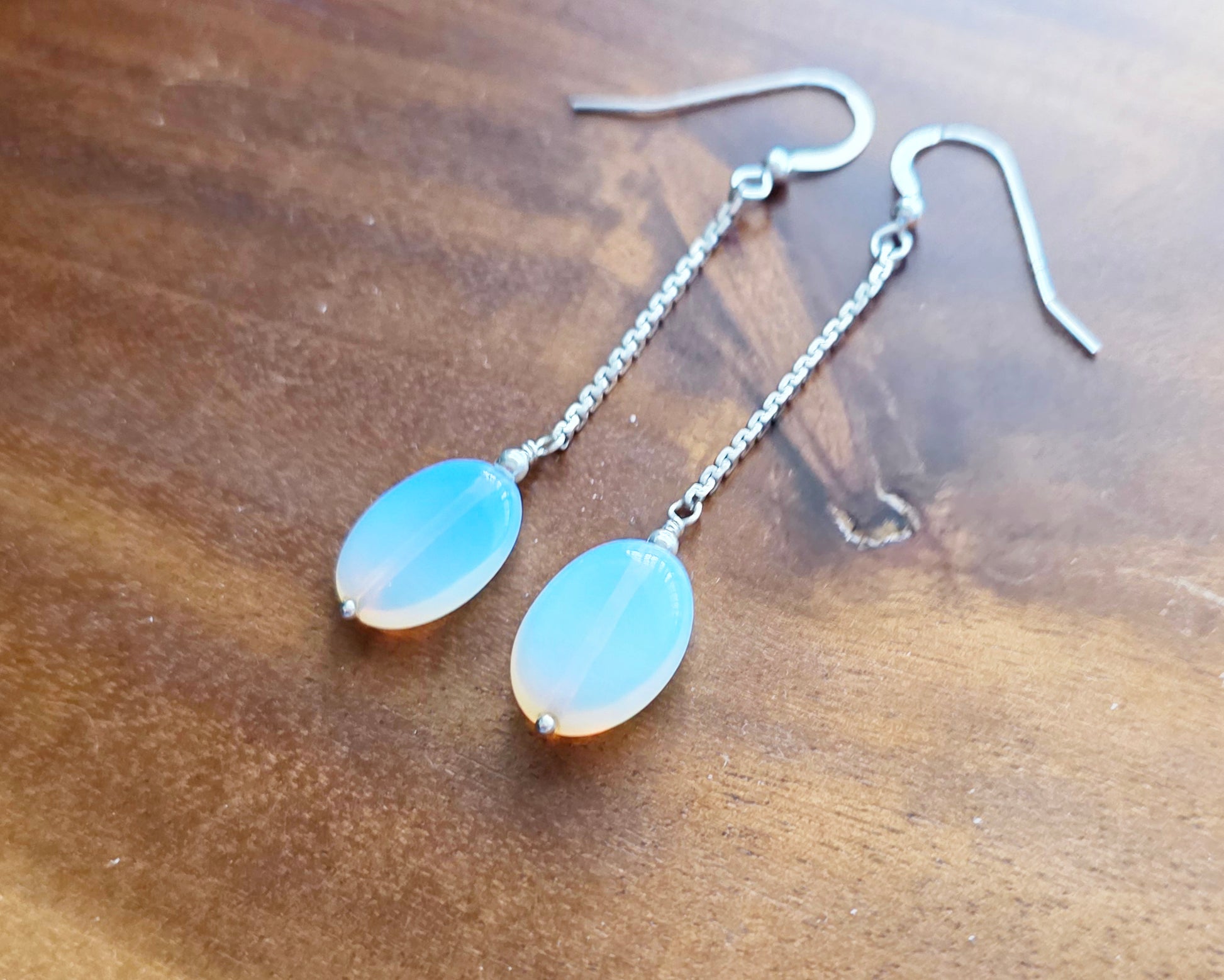 Long Sterling Silver Opaliate earrings with oval shaped stones dangling from long chains on wood background 