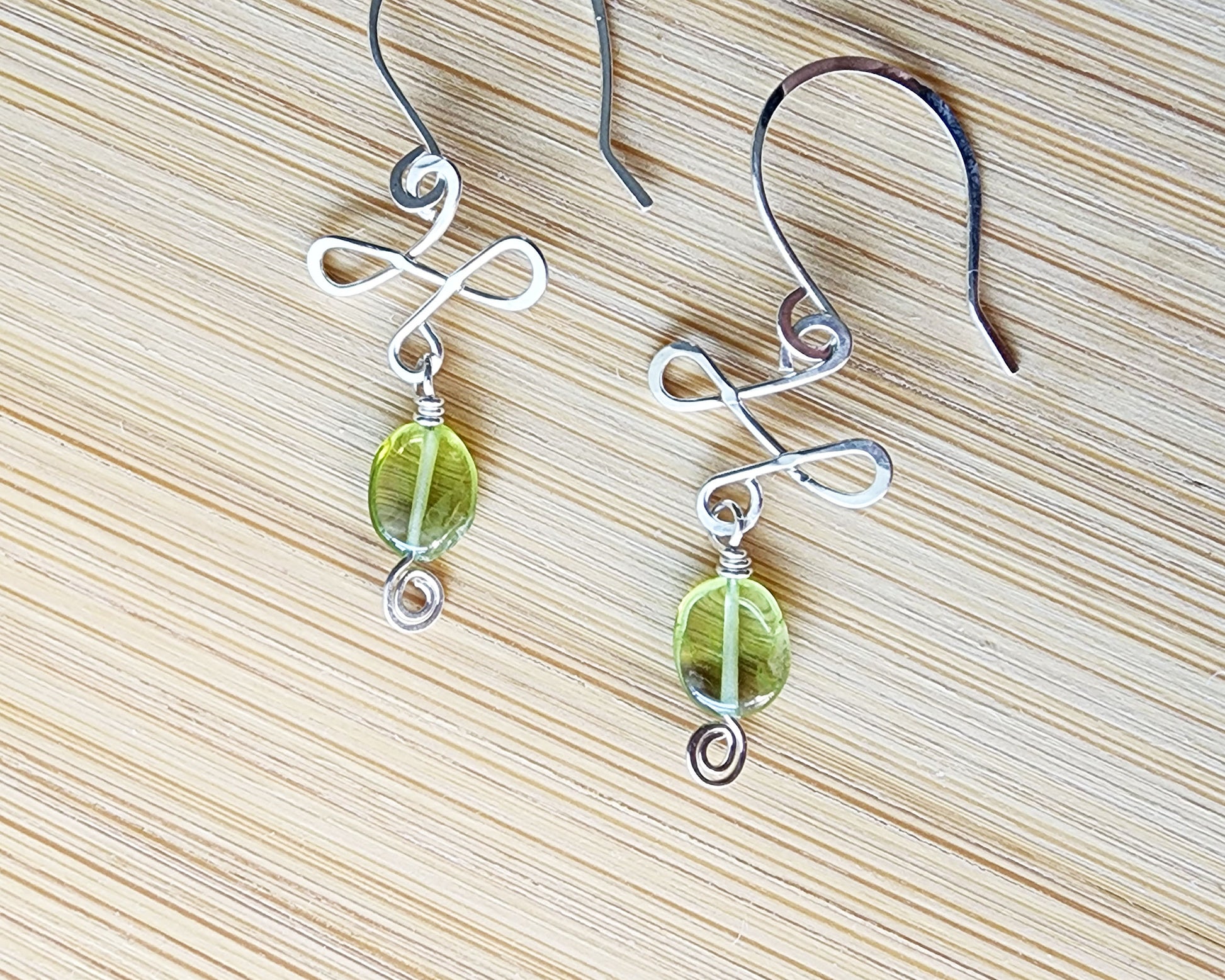 Celtic Style Peridot Dangle Earrings with Green Oval Peridot Gemstone and Sterling Silver, with Coils and French style earring hooks on wood background 