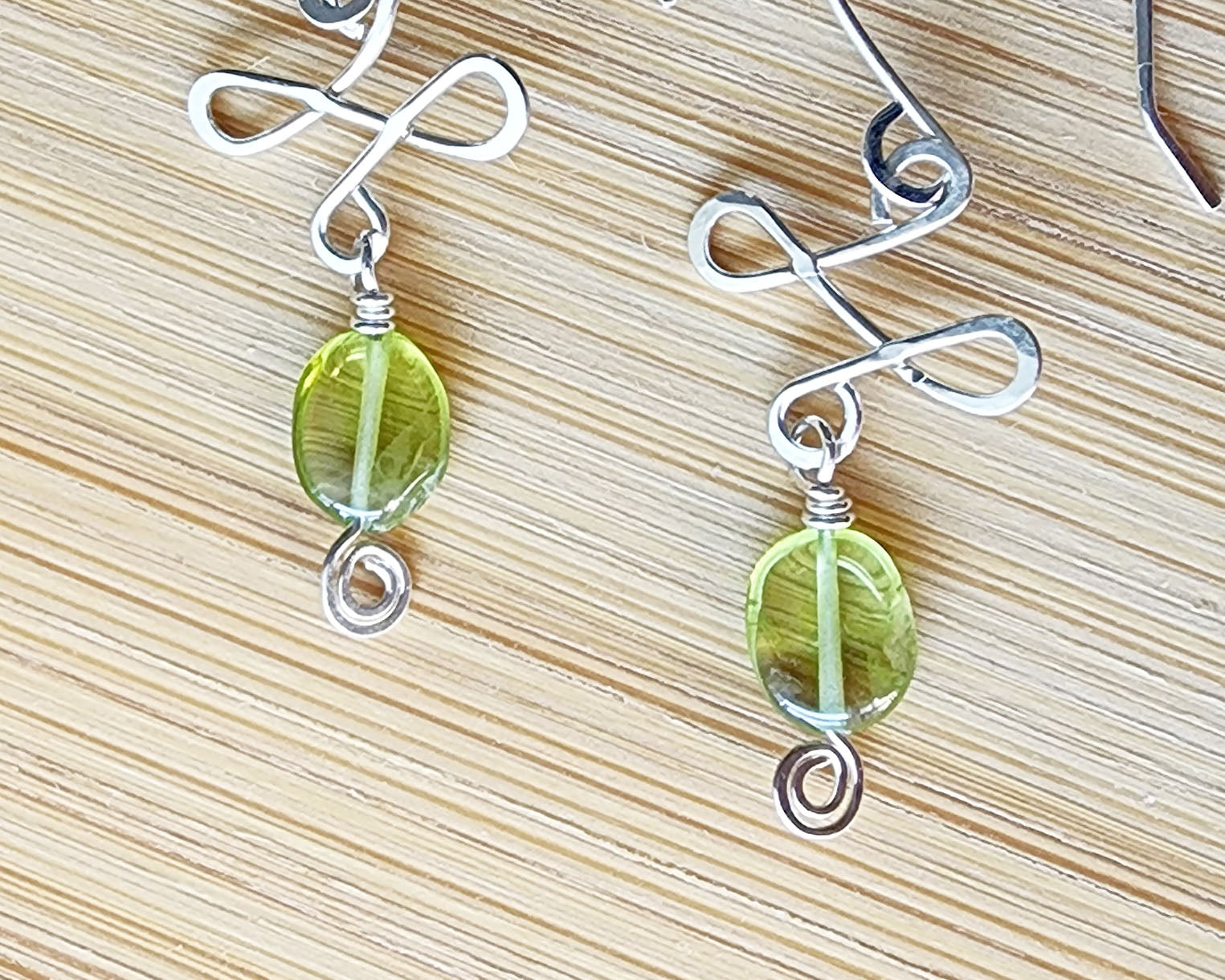 A pair of Celtic Style Peridot Dangle Earrings with Green Oval Peridot Gemstone and Sterling Silver, with Coils on wood background 