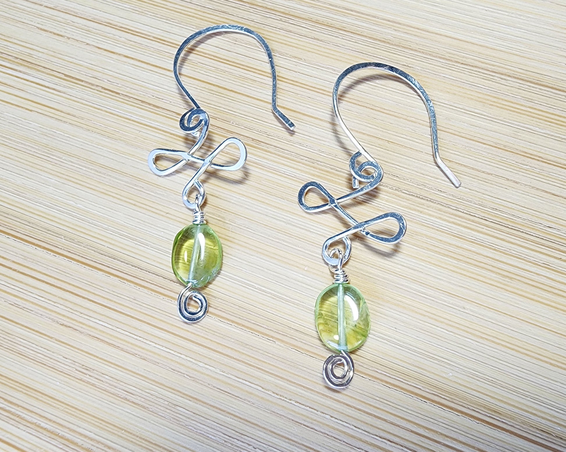 Celtic Style Peridot Dangle Earrings with Green Oval Peridot Gemstone and Sterling Silver, with Coils and French style earring hooks on wood background 