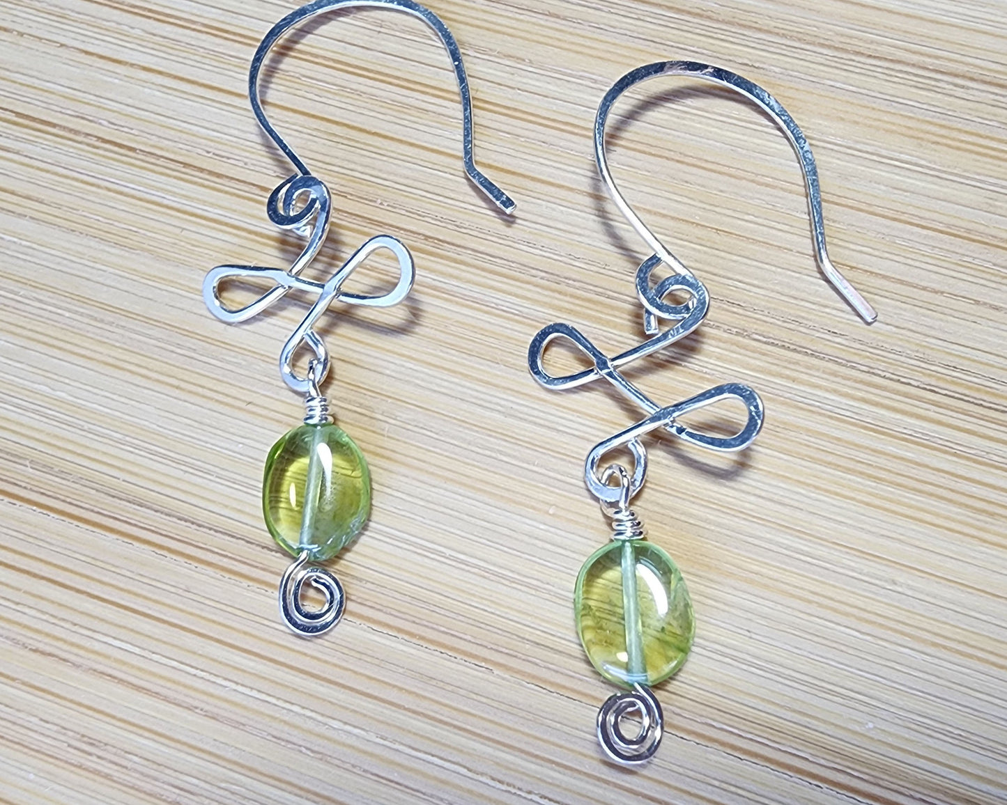 Celtic Style Peridot Dangle Earrings with Green Oval Peridot Gemstone and Sterling Silver, with Coils and French style earring hooks on wood background 