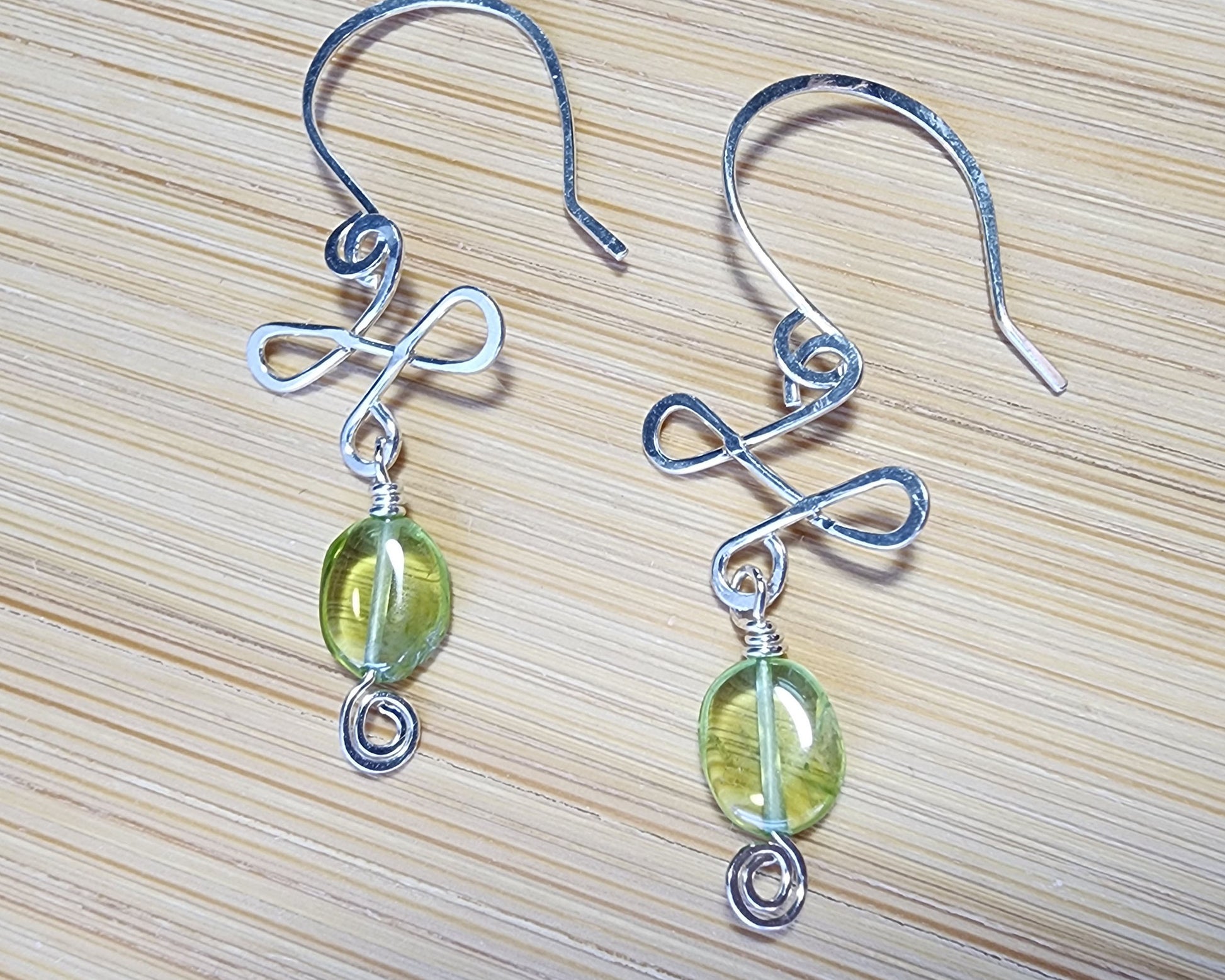 Celtic Style Peridot Dangle Earrings with Green Oval Peridot Gemstone and Sterling Silver, with Coils and French style earring hooks on wood background 
