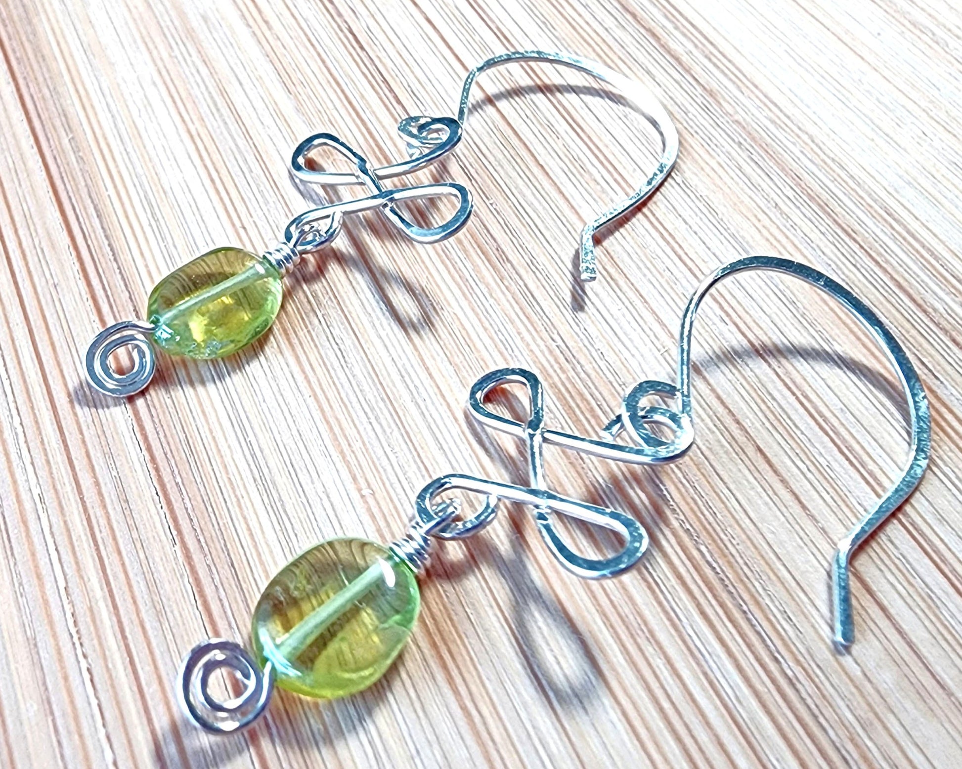 Celtic Style Peridot Dangle Earrings with Green Oval Peridot Gemstone and Sterling Silver, with Coils and French style earring hooks on wood background 