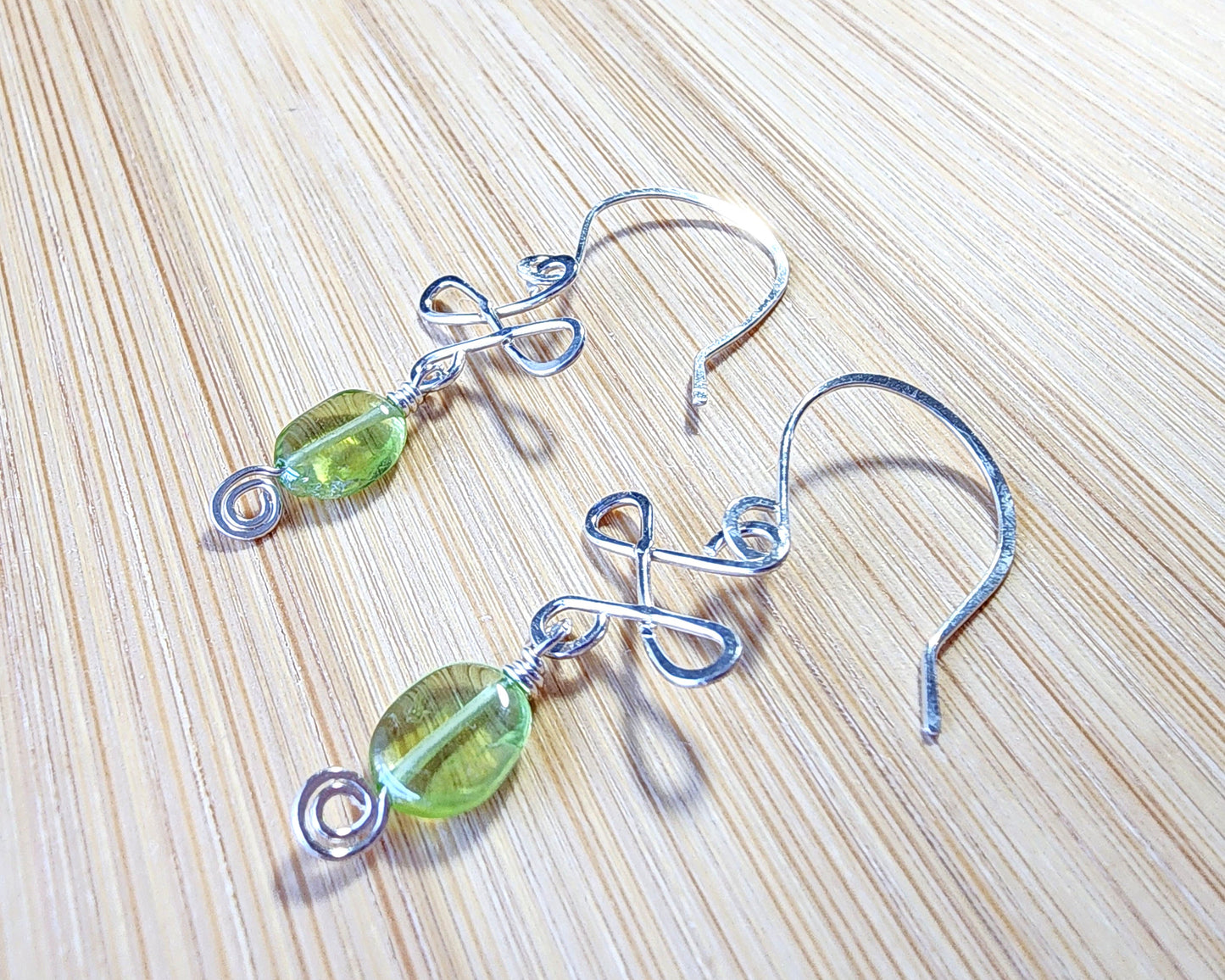 Celtic Style Peridot Dangle Earrings with Green Oval Peridot Gemstone and Sterling Silver, with Coils and French style earring hooks on wood background 