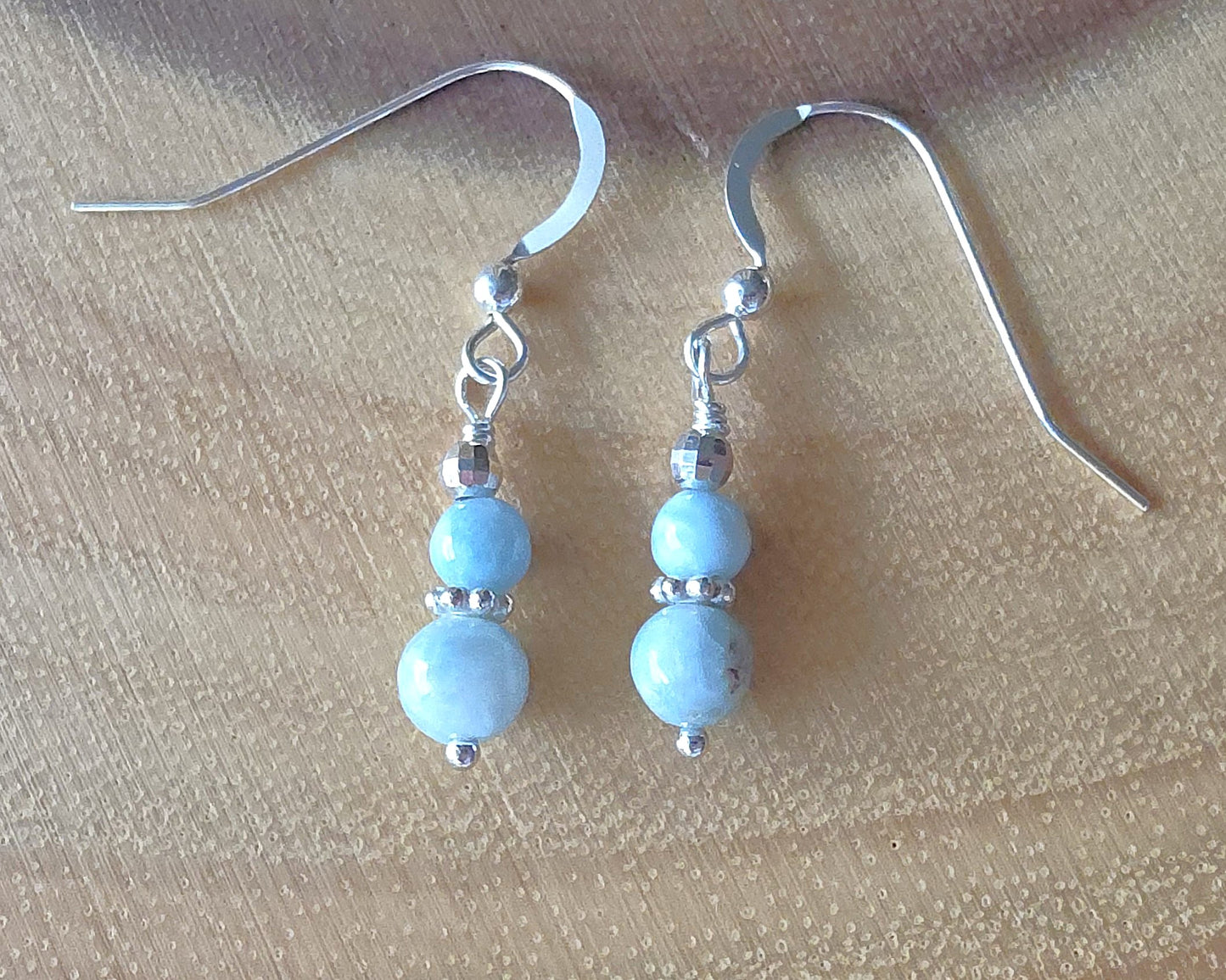 A pair of pale blue gemstone sterling silver dangle earrings on french earring hooks on wood