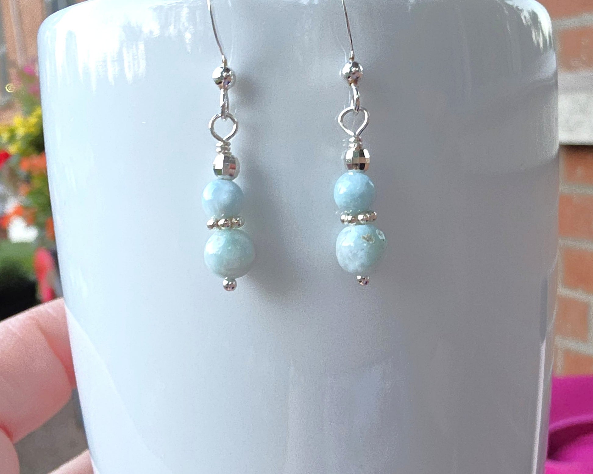 A pair of pale blue gemstone sterling silver dangle earrings on french earring hooks on white 