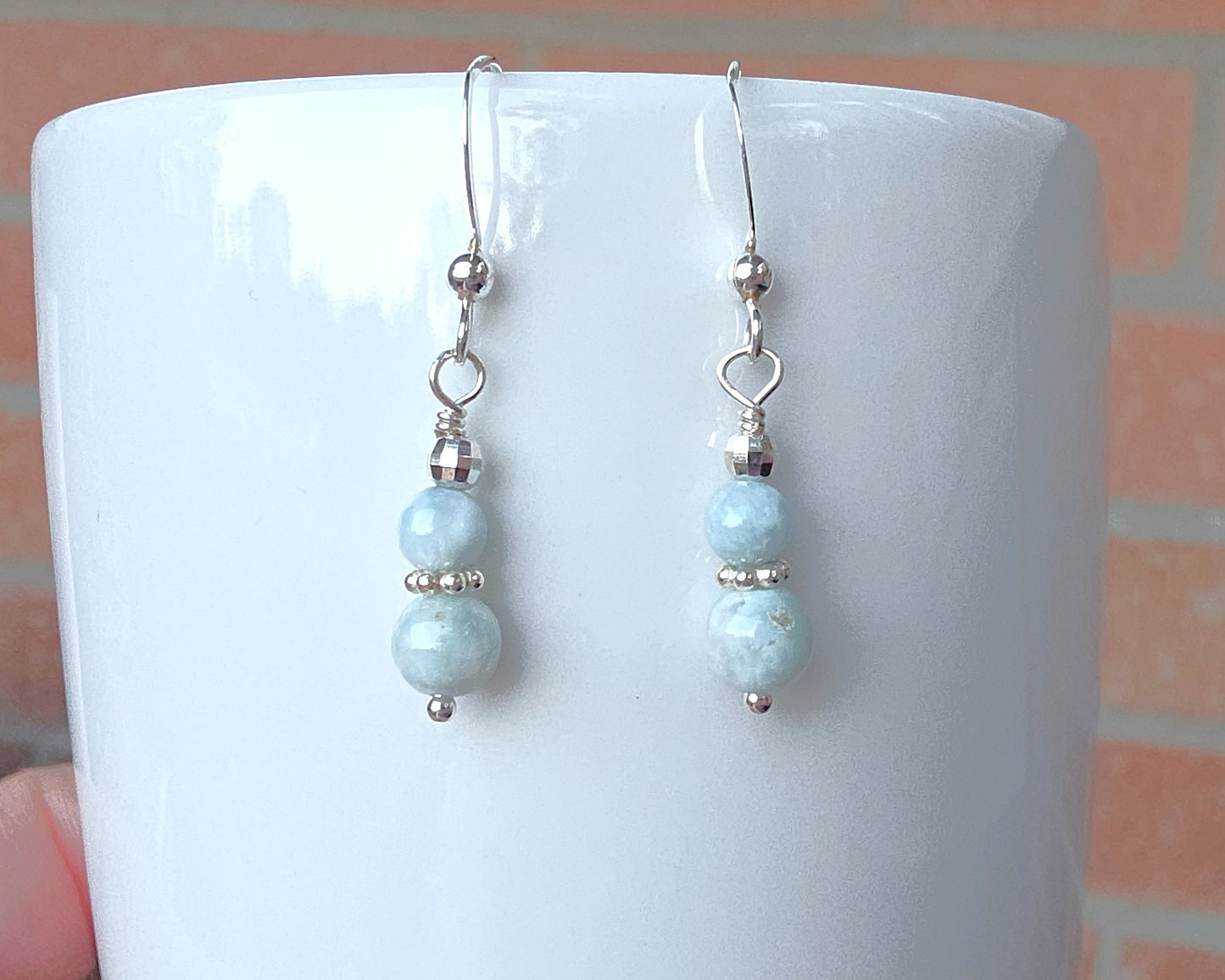 A pair of pale blue gemstone sterling silver dangle earrings on french earring hooks on white 