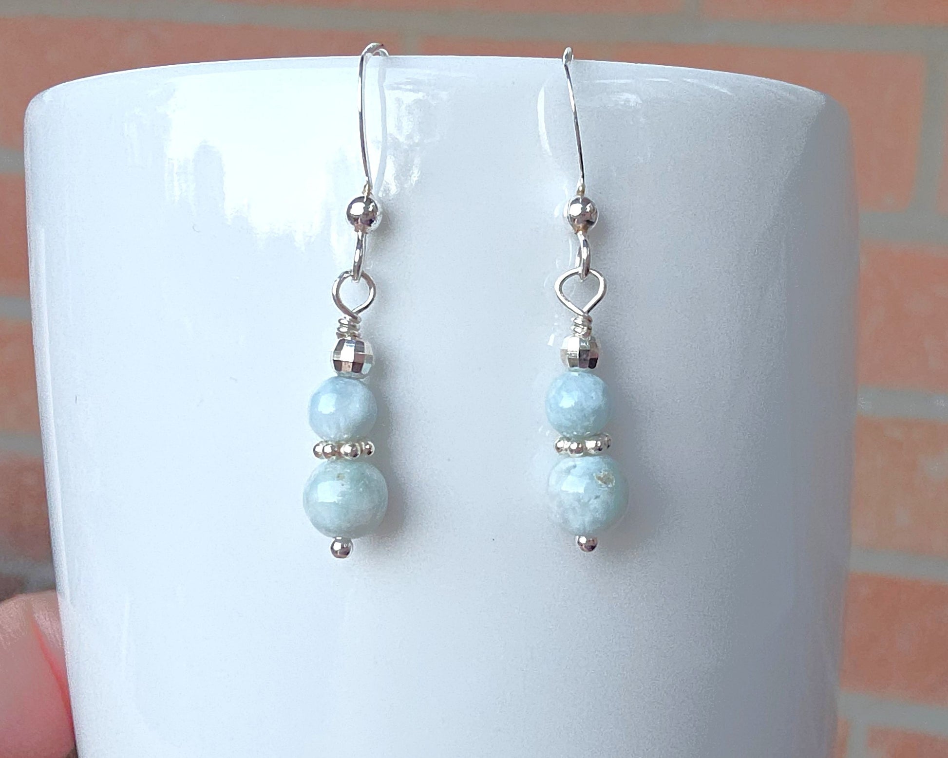 A pair of pale blue gemstone sterling silver dangle earrings on french earring hooks on white 