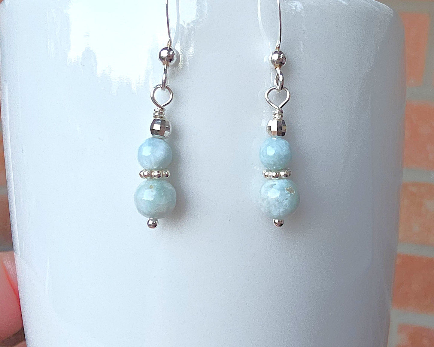 A pair of pale blue gemstone sterling silver dangle earrings on french earring hooks on white 