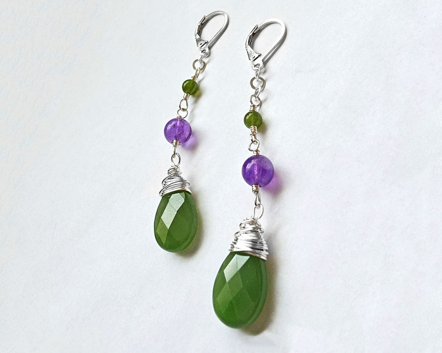 A pair of handmade long dangle drop earrings with green and purple stones, a drop shape Green Jade, wire wrapped with Amethyst and smaller Jade beads on Lever Back earring hooks on white background