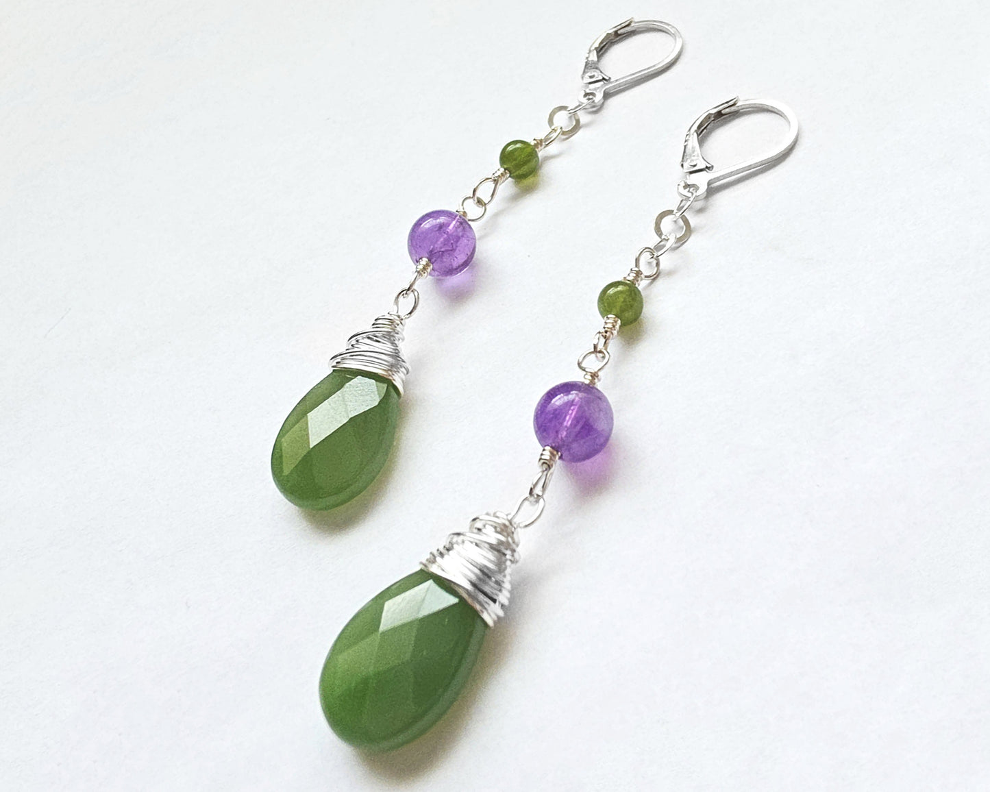 A pair of handmade long dangle drop earrings with green and purple stones, a drop shape Green Jade, wire wrapped with Amethyst and smaller Jade beads on Lever Back earring hooks on white background