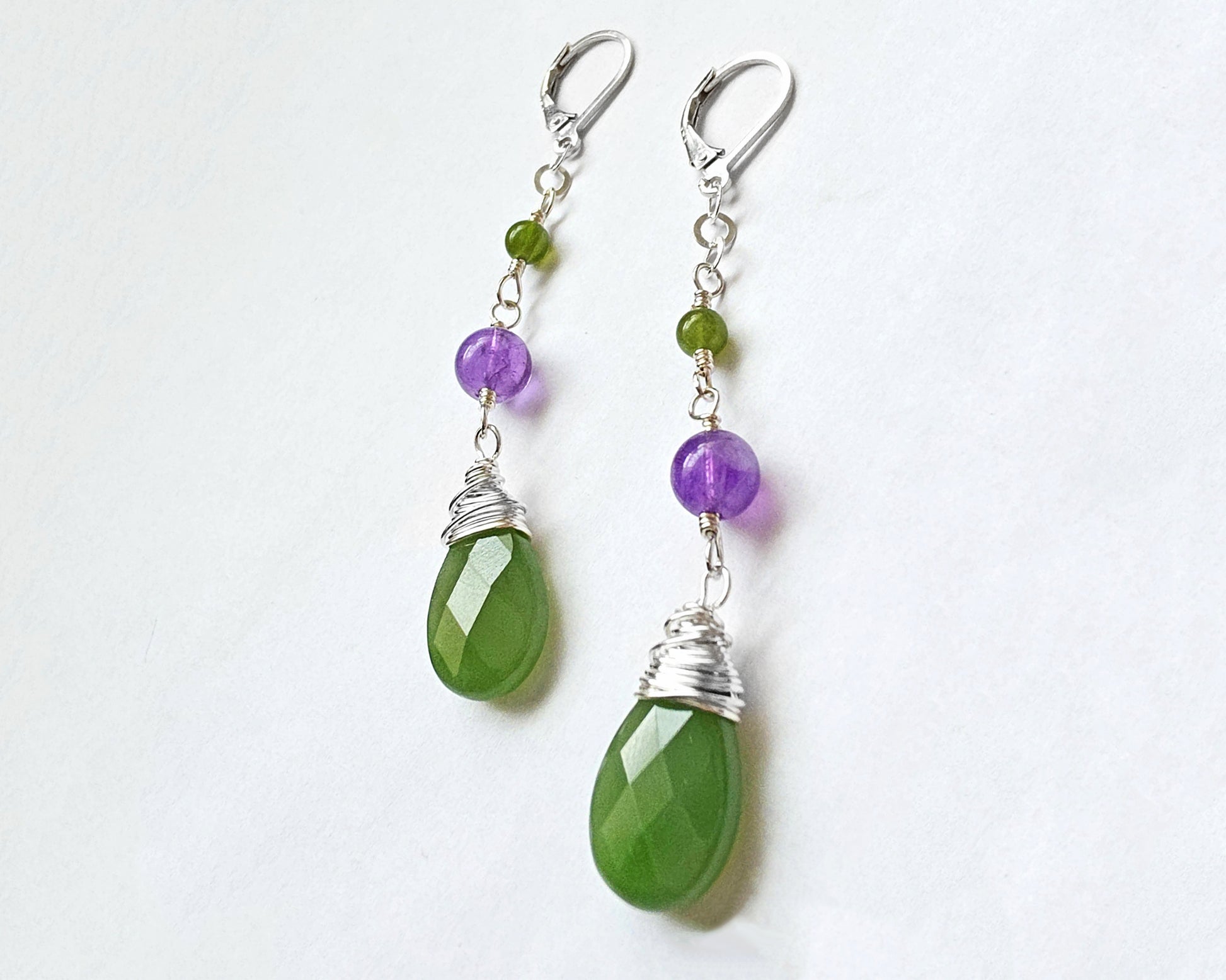 A pair of handmade long dangle drop earrings with green and purple stones, a drop shape Green Jade, wire wrapped with Amethyst and smaller Jade beads on Lever Back earring hooks on white background