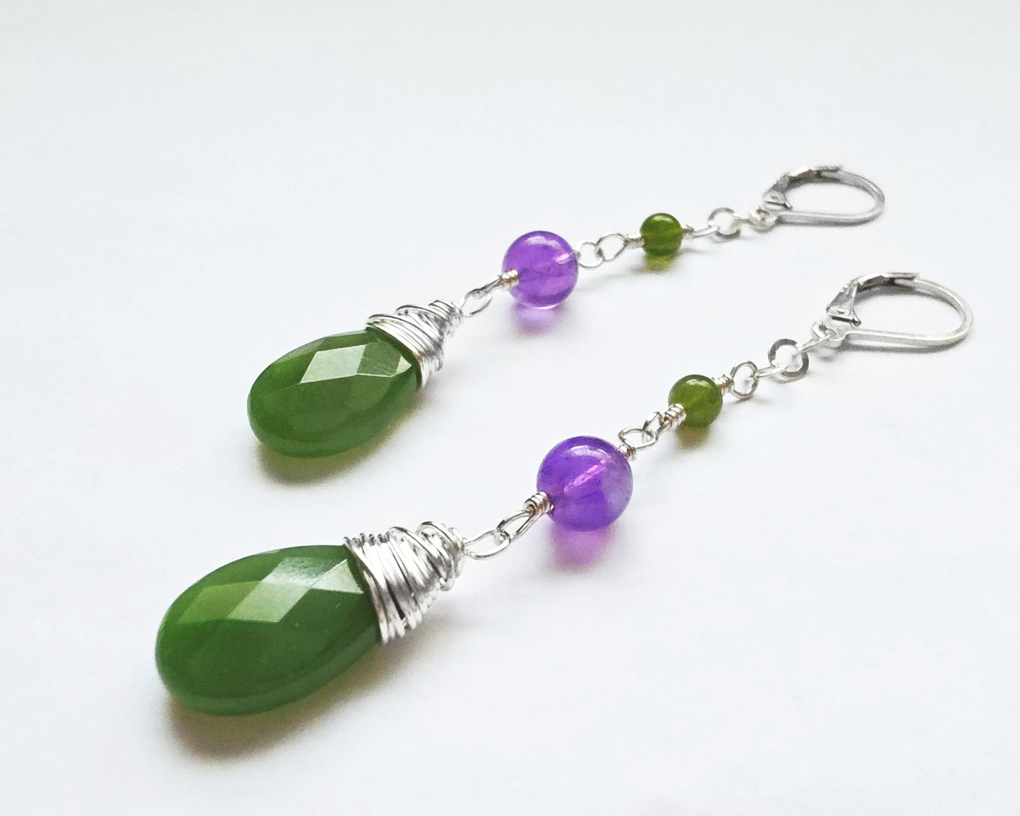 A pair of handmade long dangle drop earrings with green and purple stones, a drop shape Green Jade, wire wrapped with Amethyst and smaller Jade beads on Lever Back earring hooks on white background