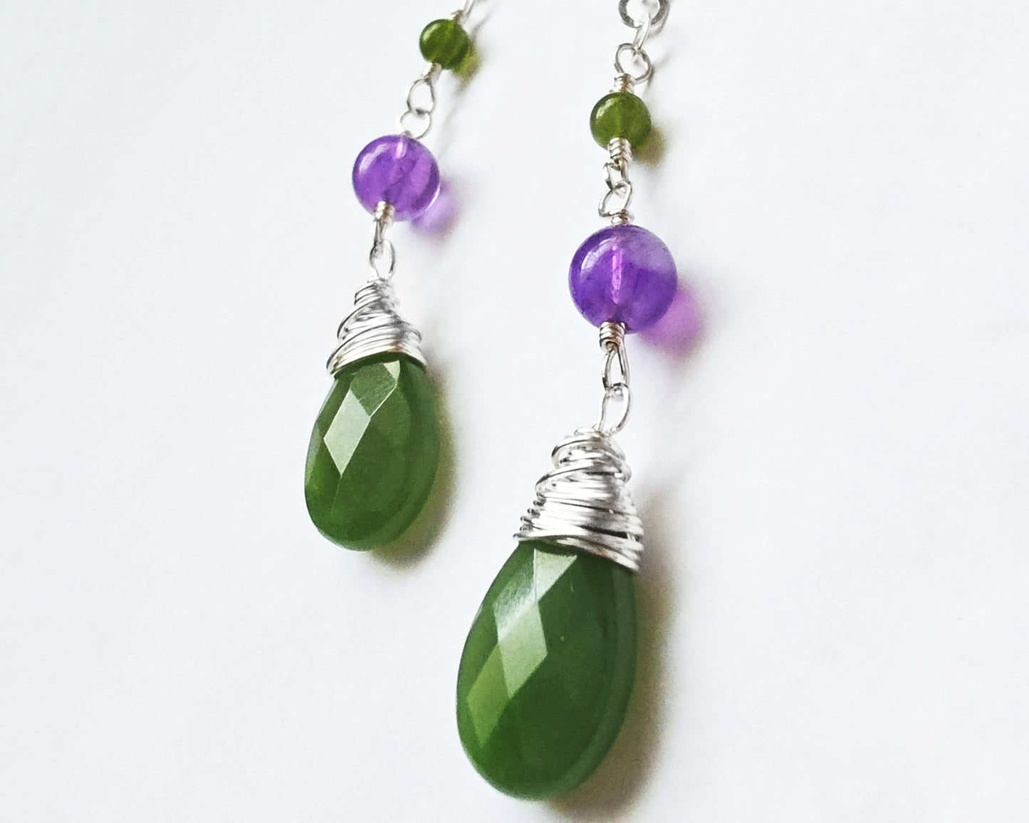 A pair of handmade long dangle drop earrings with green and purple stones, a drop shape Green Jade, wire wrapped with Amethyst and smaller Jade beads on Lever Back earring hooks on white background