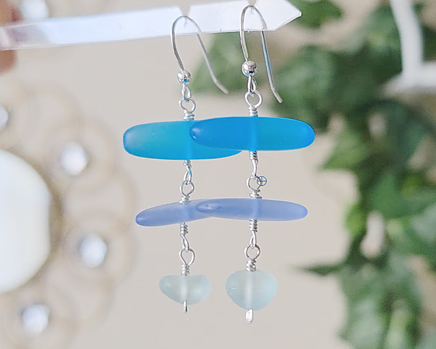 : Long Silver Sea glass earrings with three different colors of blue glass from aqua to sky blue on french style earring hooks with plants in the background 
