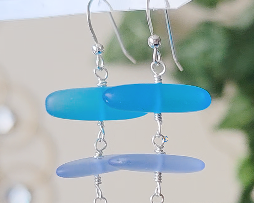 : Long Silver Sea glass earrings with three different colors of blue glass from aqua to sky blue on french style earring hooks with plants in the background 