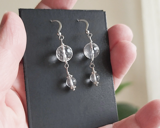 A pair of clear Quartz Crystal Earrings with faceted and polished stones with Sterling Silver beads, wire wrapped and french hooks on black card and hand
