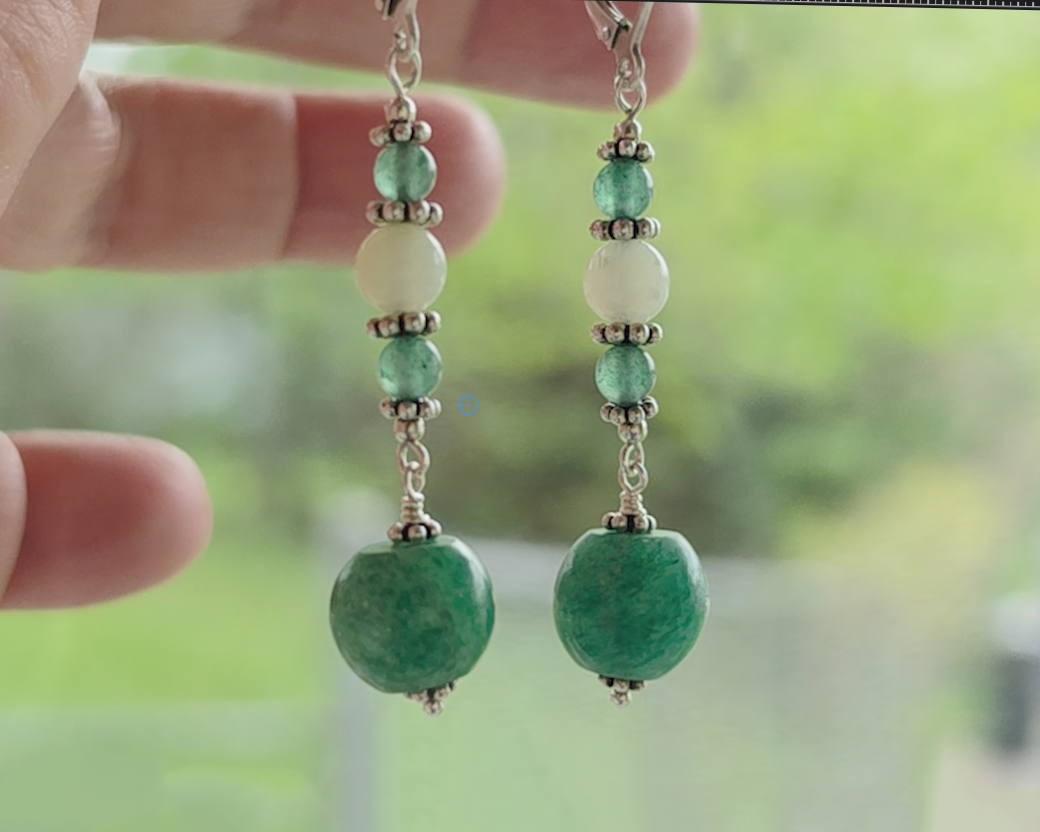 Long green gemstone earrings with deeper green aventurine and pale green jade with decorative sterling silver beads with blurred trees in background