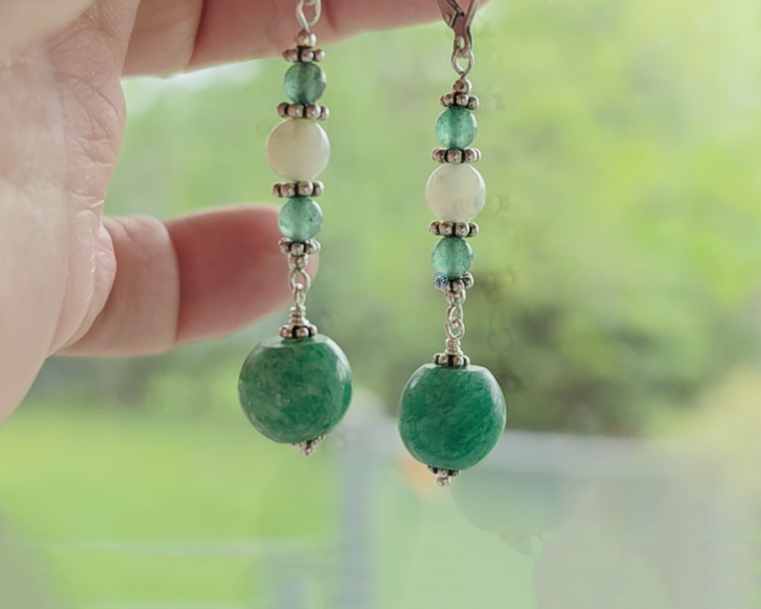 Long green gemstone earrings with deeper green aventurine and pale green jade with decorative sterling silver beads with blurred trees in background