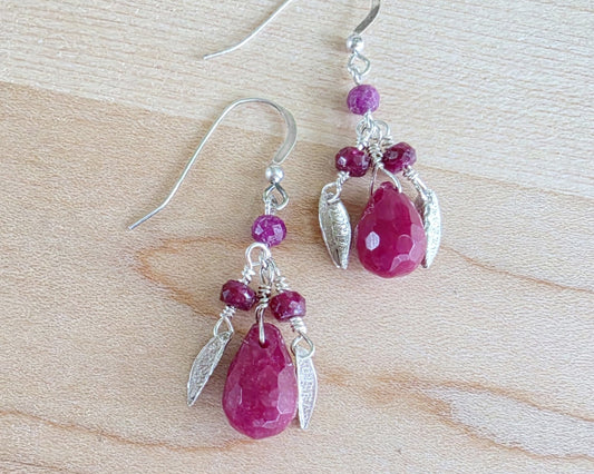 A pair of handmade Ruby earrings with Sterling Silver leaf’s, large drop shape red gemstone and red rubies with french earring hooks on light color wood