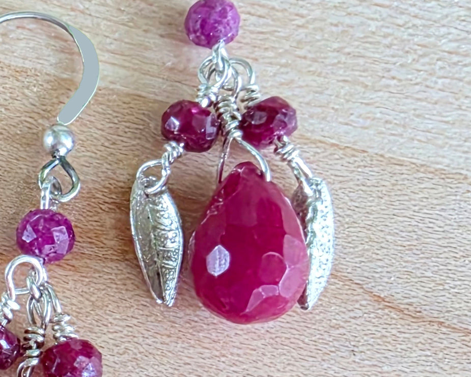 A pair of handmade Ruby earrings with Sterling Silver leaf’s, large drop shape red gemstone and red rubies with french earring hooks on light color wood