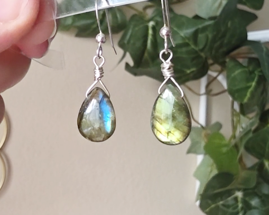 Handmade Labradorite drop shaped earrings with colorful flashes of blue and gold on sterling silver french hooks with plants in the background 