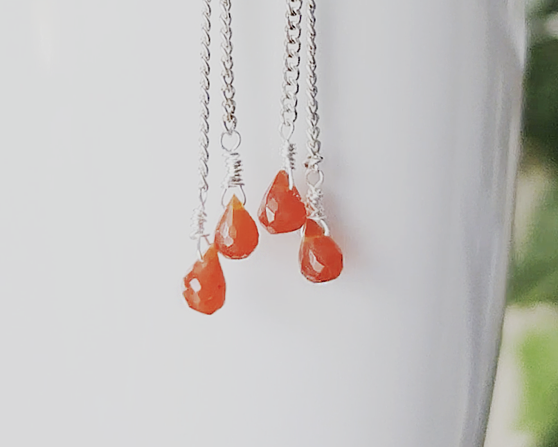A pair of handmade long dangle earrings with orange faceted Carnelian drop shaped stones dangling from Sterling Silver chain on white background