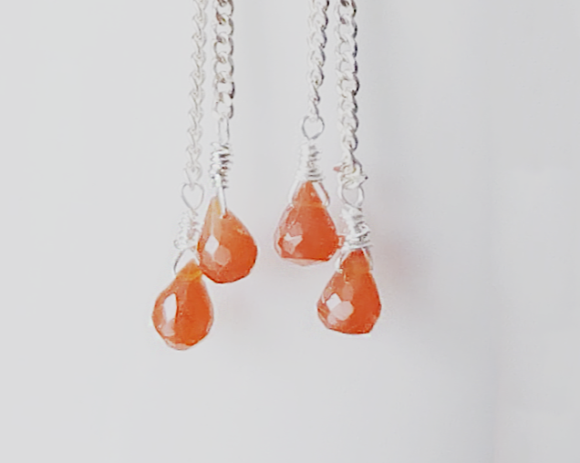 A pair of handmade long dangle earrings with orange faceted Carnelian drop shaped stones dangling from Sterling Silver chain on white background