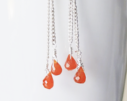 A pair of handmade long dangle earrings with orange faceted Carnelian drop shaped stones dangling from Sterling Silver chain on white background