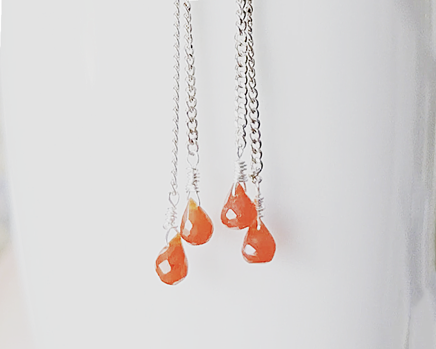 A pair of handmade long dangle earrings with orange faceted Carnelian drop shaped stones dangling from Sterling Silver chain on white background