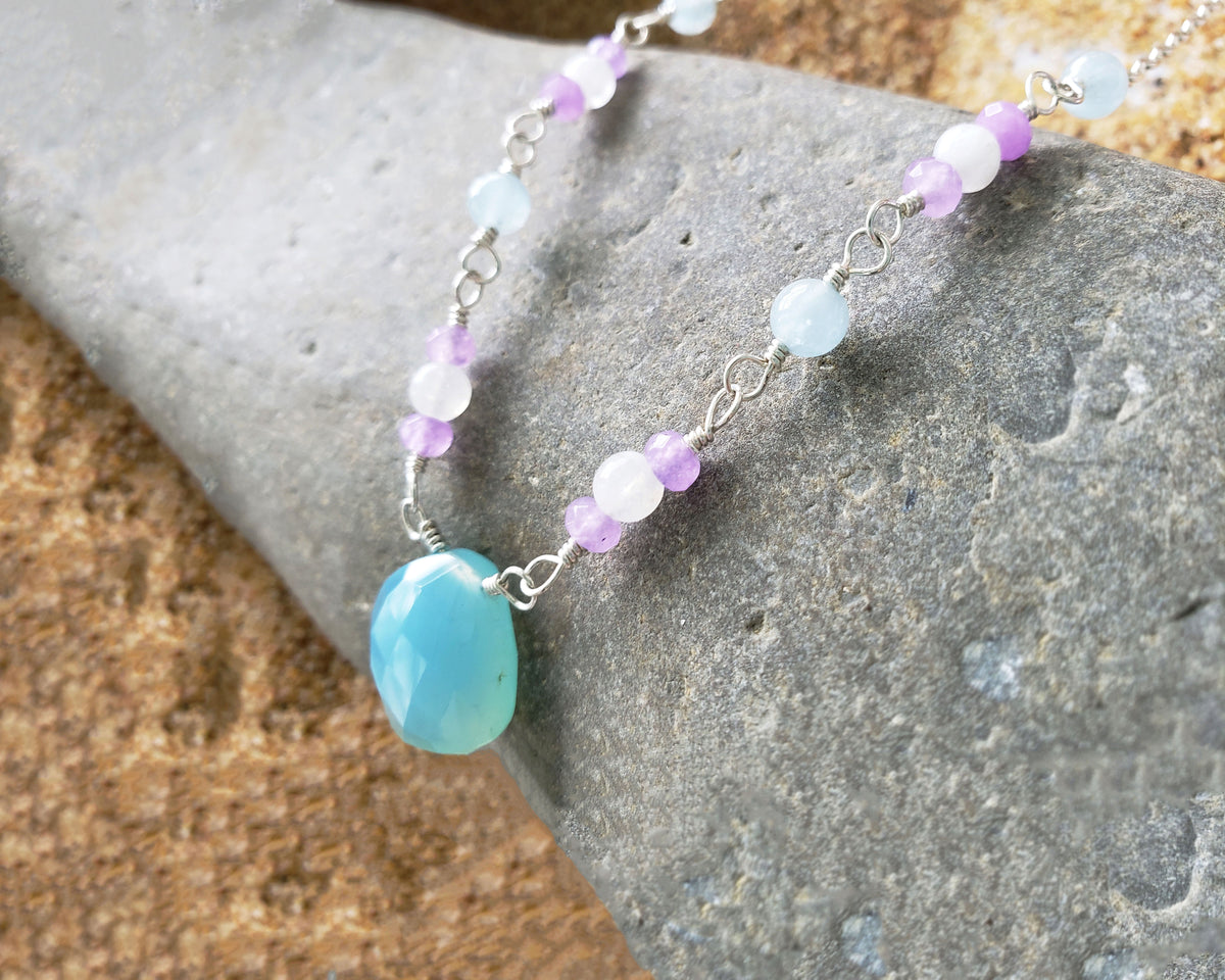 Handmade Blue, Lavender and white Blue Chalcedony, Moonstone, Aquamarine, Lavender Quartz, Sterling Silver wire wrapped necklace with large blue stone in with gray stone background 