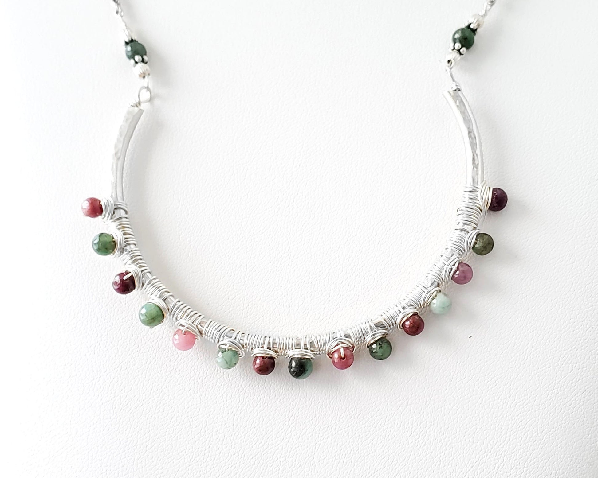 Sterling Silver Necklace with Rubies and Emerald, a wire wrapped curved pendant on white background 