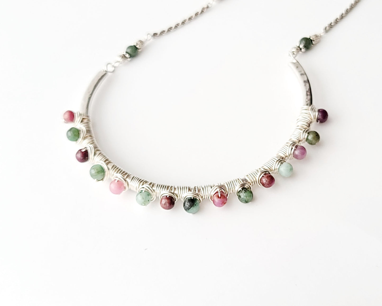 Sterling Silver Necklace with Rubies and Emerald, a wire wrapped curved pendant on white background 