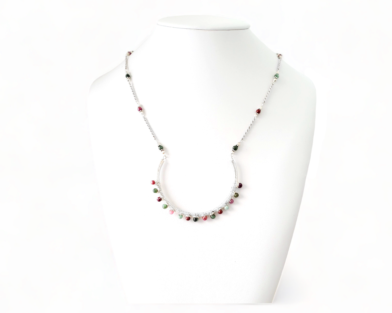 Sterling Silver Necklace with Rubies and Emerald, a wire wrapped curved pendant on white background 