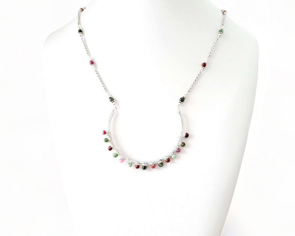 Sterling Silver Necklace with Rubies and Emerald, a wire wrapped curved pendant on white background 