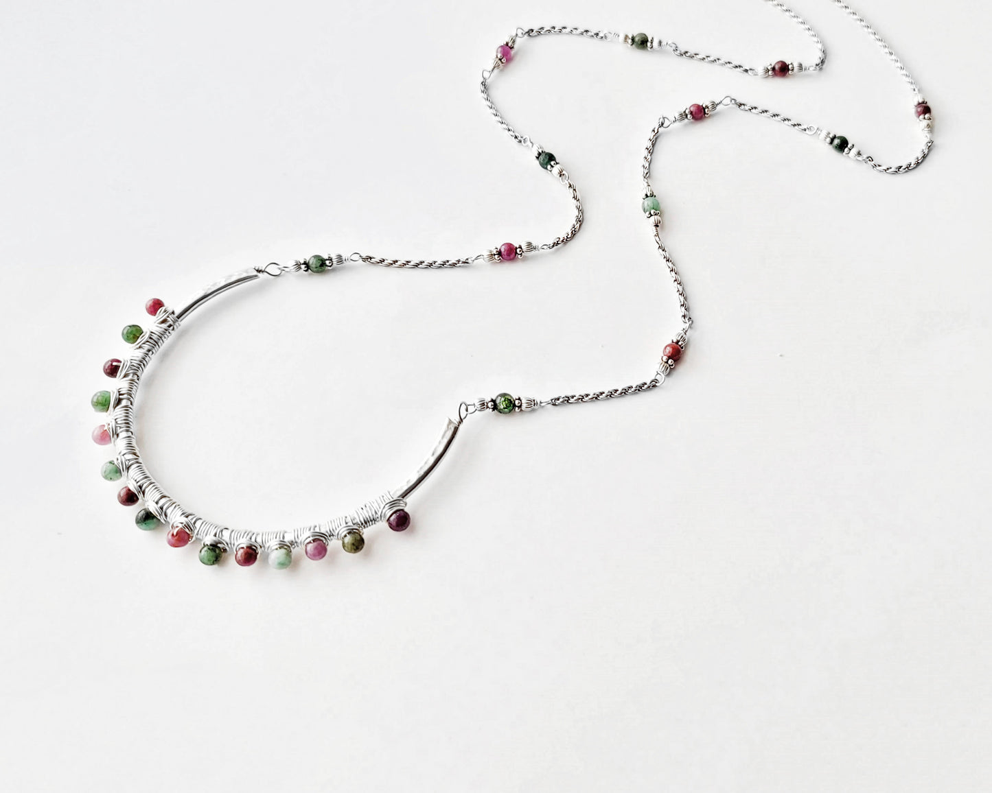 Sterling Silver Necklace with Rubies and Emerald, a wire wrapped curved pendant on white background 