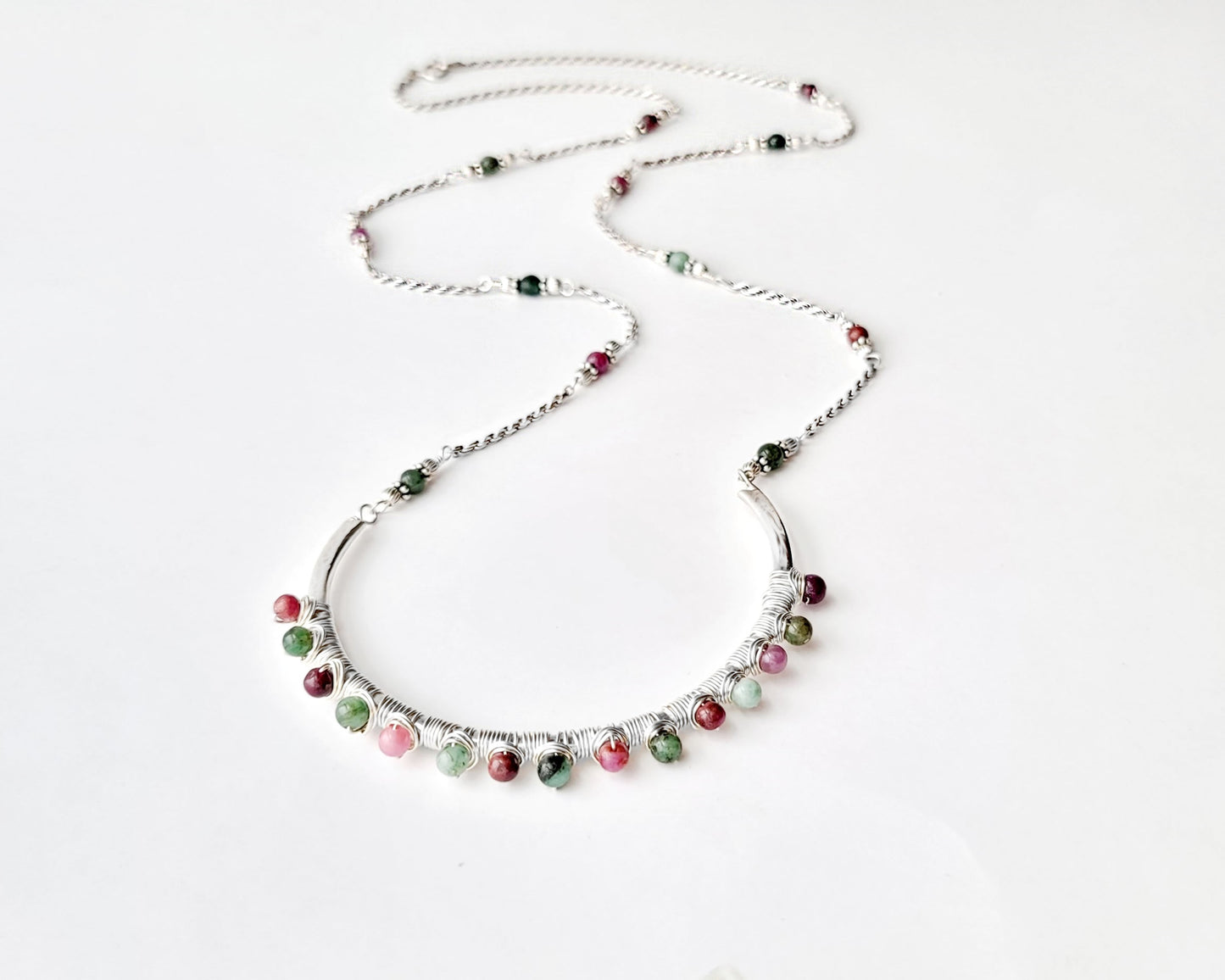 Sterling Silver Necklace with Rubies and Emerald, a wire wrapped curved pendant on white background 