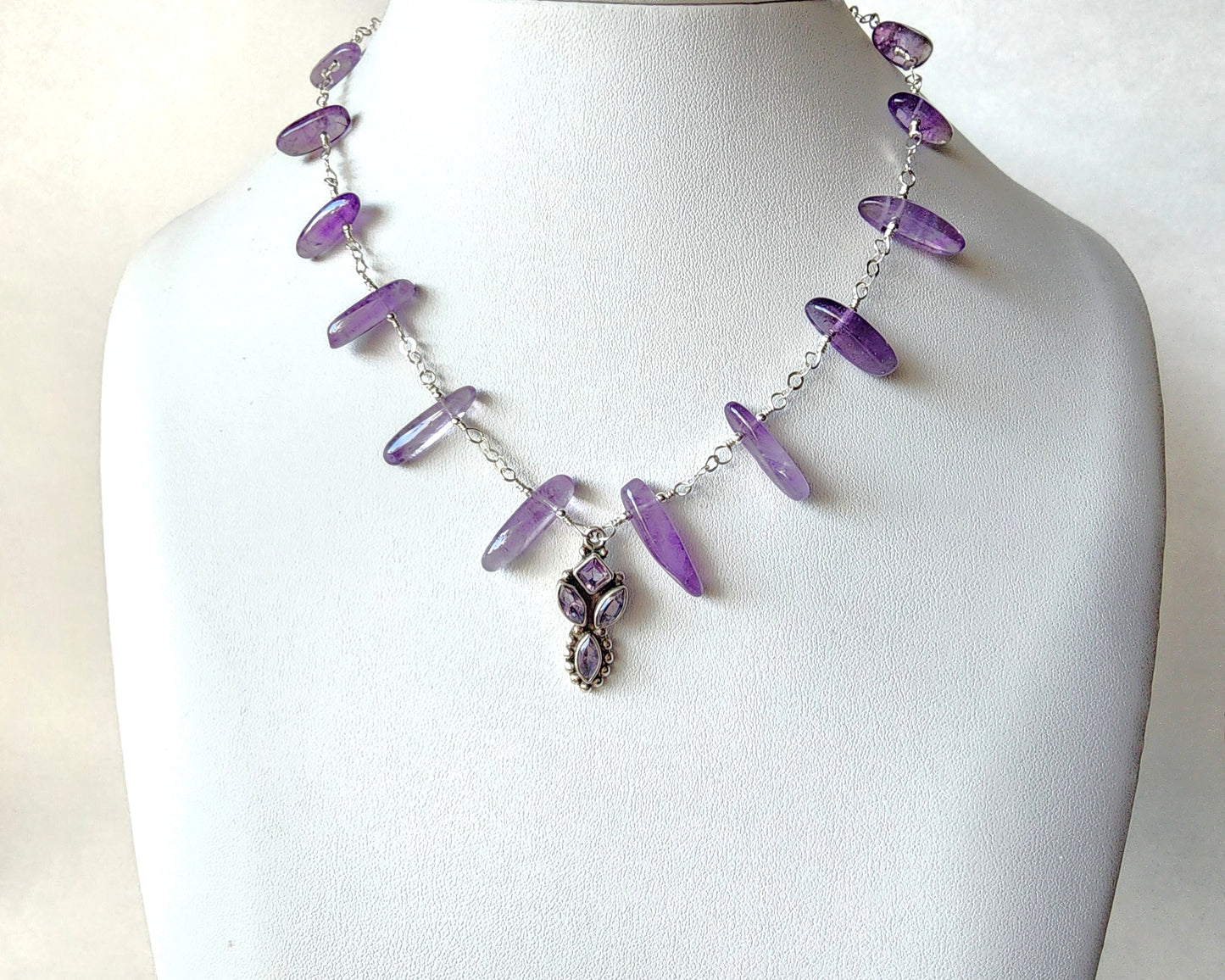 Amethyst Sterling Silver almost fan style Necklace with Decorative Silver pendant with sparkly faceted stones and wire wrapped long stones and silver chain on white display bust
