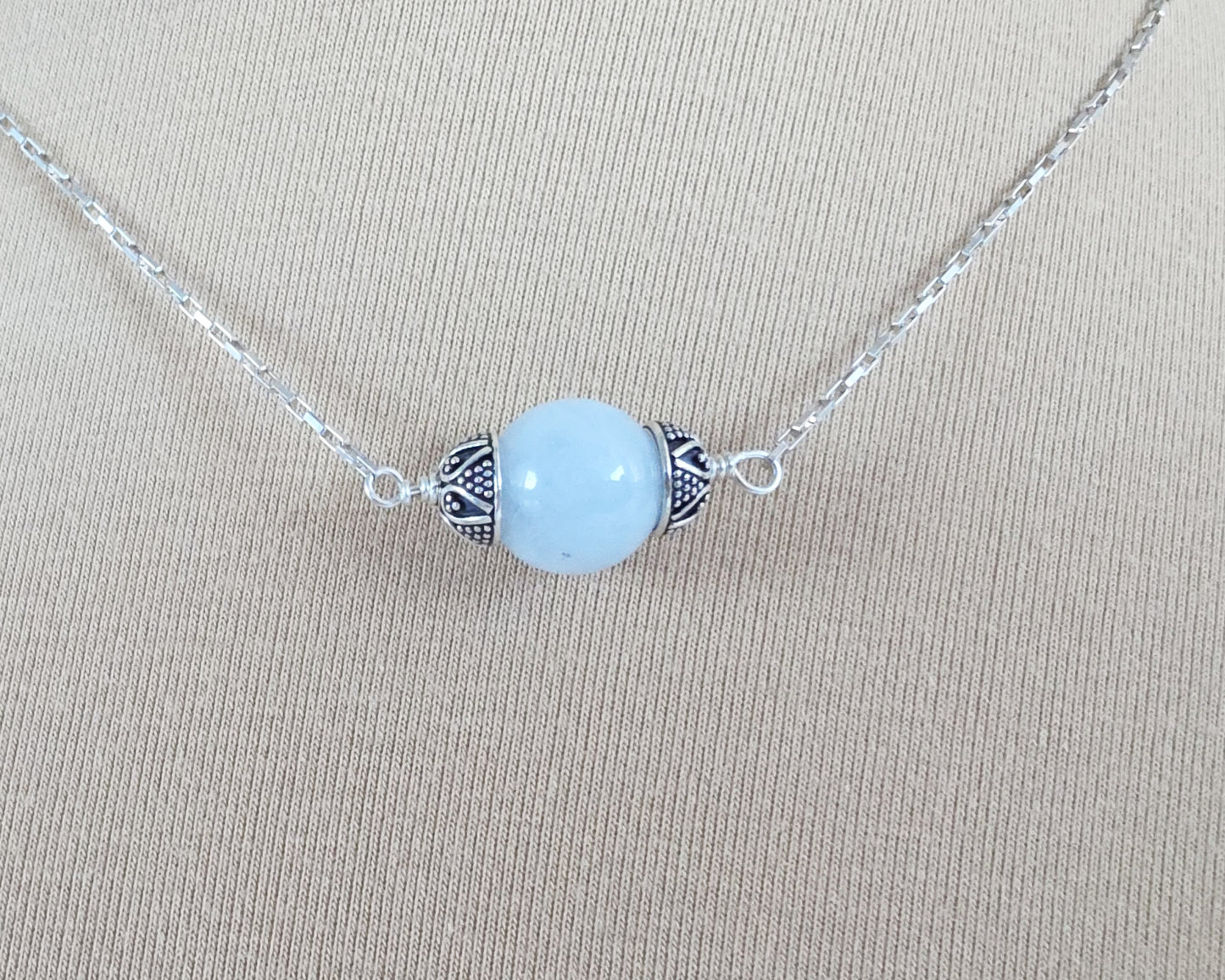 Aquamarine Necklace with one large single round blue Aquamarine stone with silver caps on beige background display