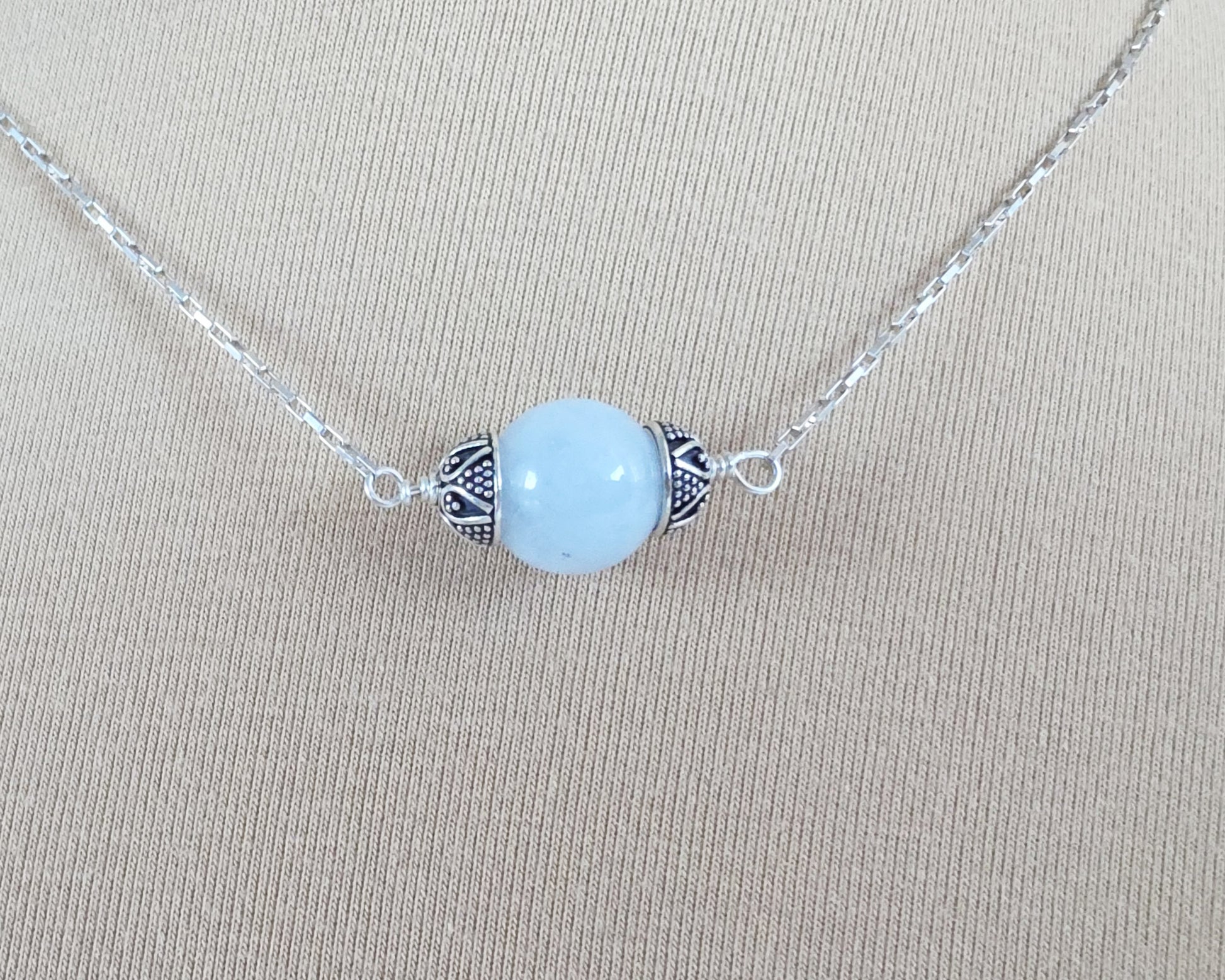 Aquamarine Necklace with one large single round blue Aquamarine stone with silver caps on beige background display