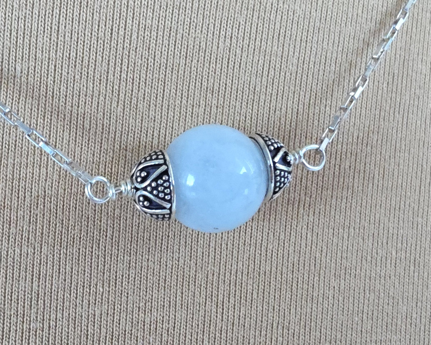 Aquamarine Necklace with one large single round blue Aquamarine stone with silver caps on beige background 