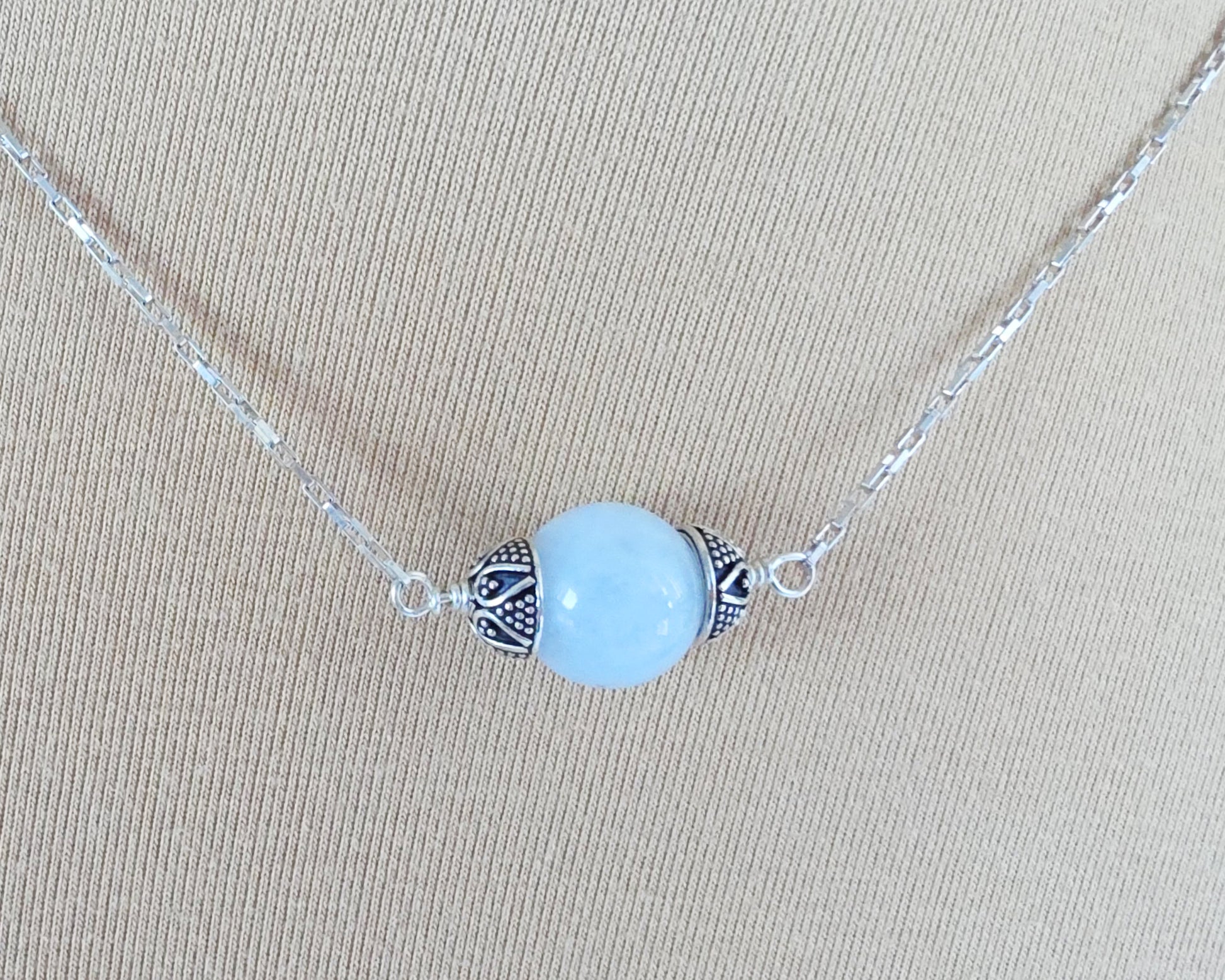 Aquamarine Necklace with one large single round blue Aquamarine stone with silver caps on beige background display