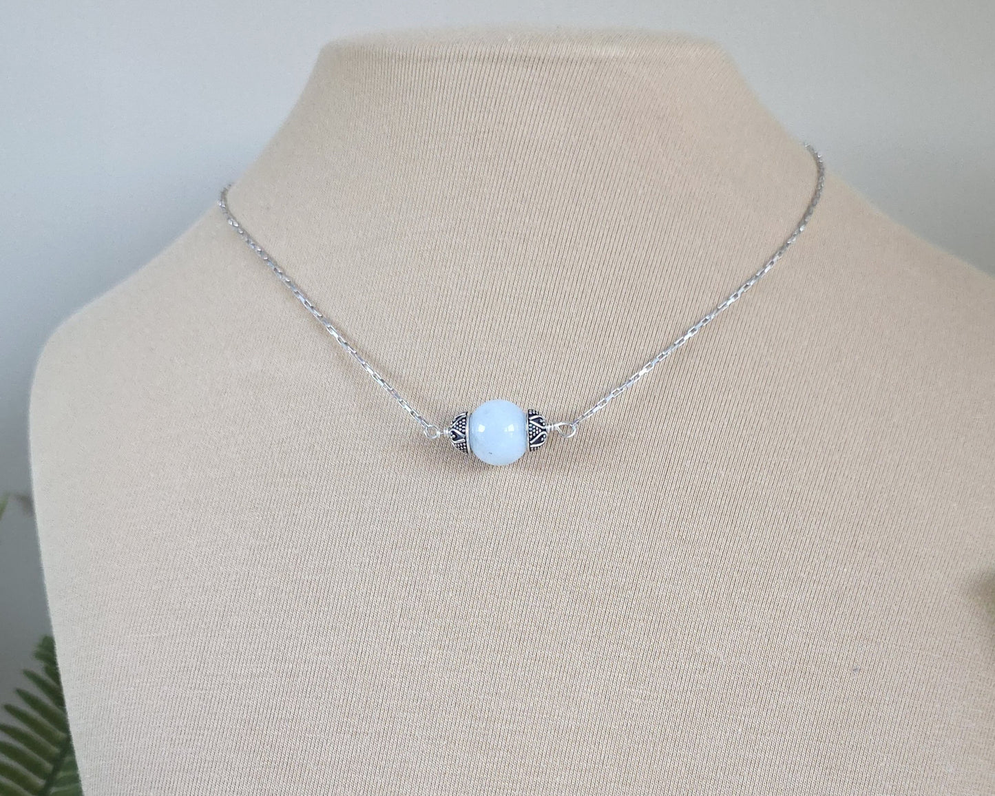 Aquamarine Necklace with one large single round blue Aquamarine stone with silver caps on beige background display